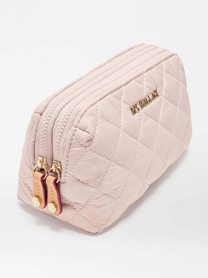 The MZ Wallace Small Double Zip Cosmetic in City Pink Oxford is a quilted light pink pouch made from REC Oxford Fabrication, with gold-tone hardware, double zip top closure, and "THE SMALL ONE" embossed in gold letters.