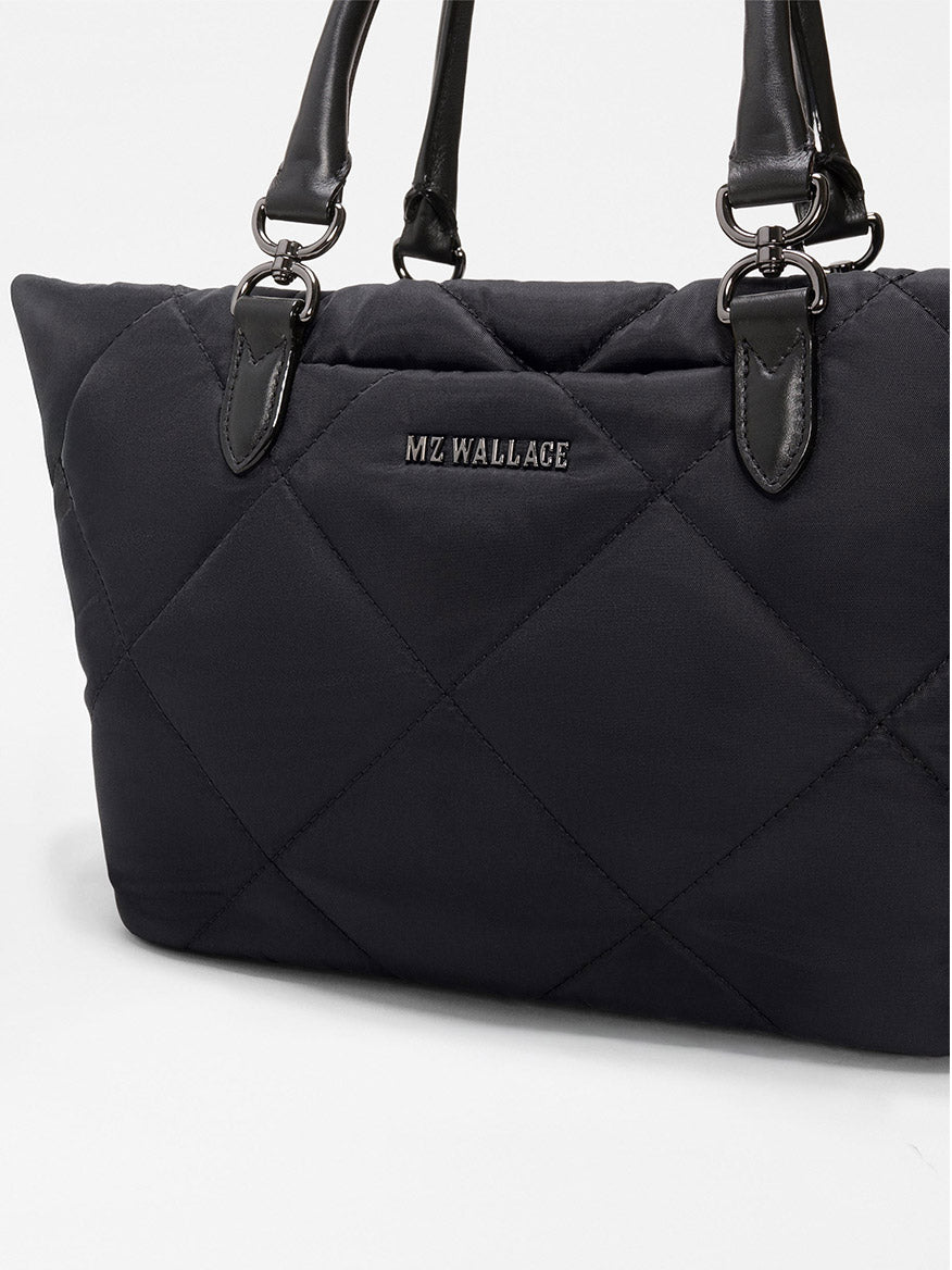 The MZ Wallace Small Madison E/W Tote in Black Bedford is a black quilted handbag with Italian leather trim, black handles, metal hardware, a slim east–west silhouette, and the "MZ WALLACE" logo on the front.