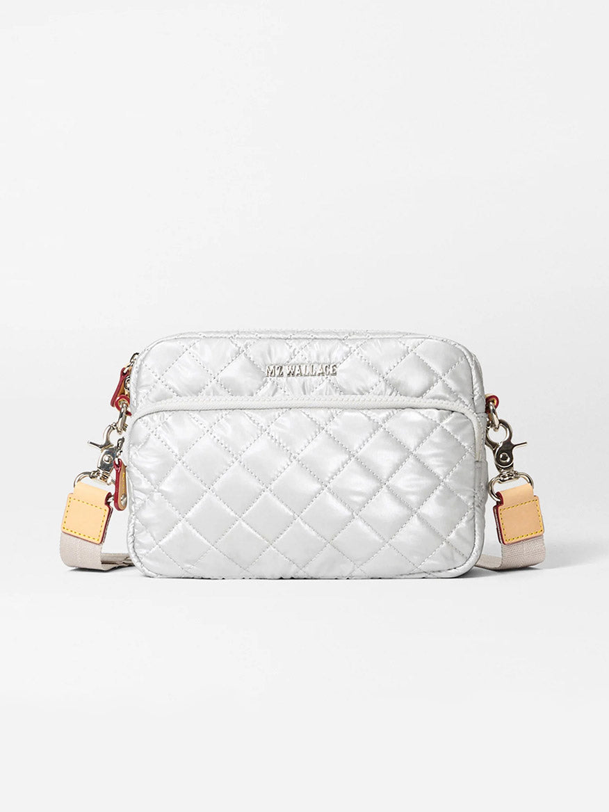 The MZ Wallace Small Metro Camera Bag in Oyster Metallic Oxford features quilted silver nylon, leather trim, a front zipper pocket, adjustable strap, and silver hardware, shown against a plain white background.