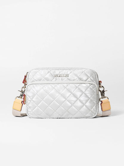 The MZ Wallace Small Metro Camera Bag in Oyster Metallic Oxford features quilted silver nylon, leather trim, a front zipper pocket, adjustable strap, and silver hardware, shown against a plain white background.