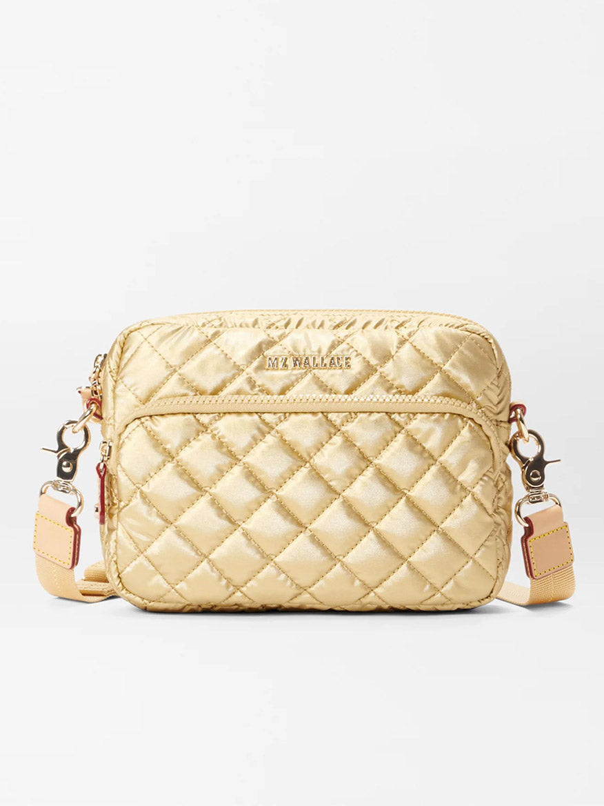 A small, quilted, rectangular beige handbag with a strap and metallic clasps, the MZ Wallace Small Metro Camera Bag in Light Gold Metallic Oxford is elegantly displayed on a white background.