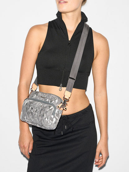 A person is wearing a black sleeveless zip-up top and black pants, with an MZ Wallace Small Metro Camera Bag in Silver Metallic Camo Oxford hanging over their shoulder.