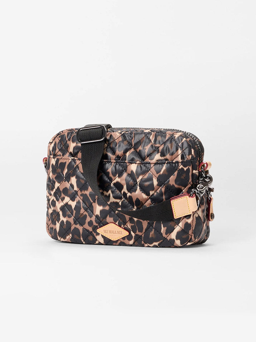 The MZ Wallace Small Metro Camera Bag in Leopard Oxford features quilted nylon with a black and brown leopard print, a black adjustable strap, and a tan leather front tag—an ideal chic camera bag or Metro Crossbody alternative.