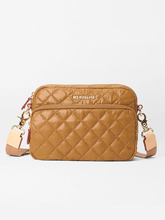 The MZ Wallace Small Metro Camera Bag in Amber Oxford features a tan quilted lightweight nylon design, gold-tone hardware, front zip pocket, adjustable strap, and "MZ WALLACE" in gold lettering on the front.