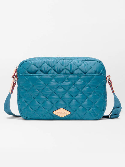 The MZ Wallace Small Metro Camera Bag in Pacific Oxford features teal quilted nylon with a diamond pattern, adjustable strap, and a tan front logo patch—a stylish, compact crossbody inspired by classic MZ Wallace design.