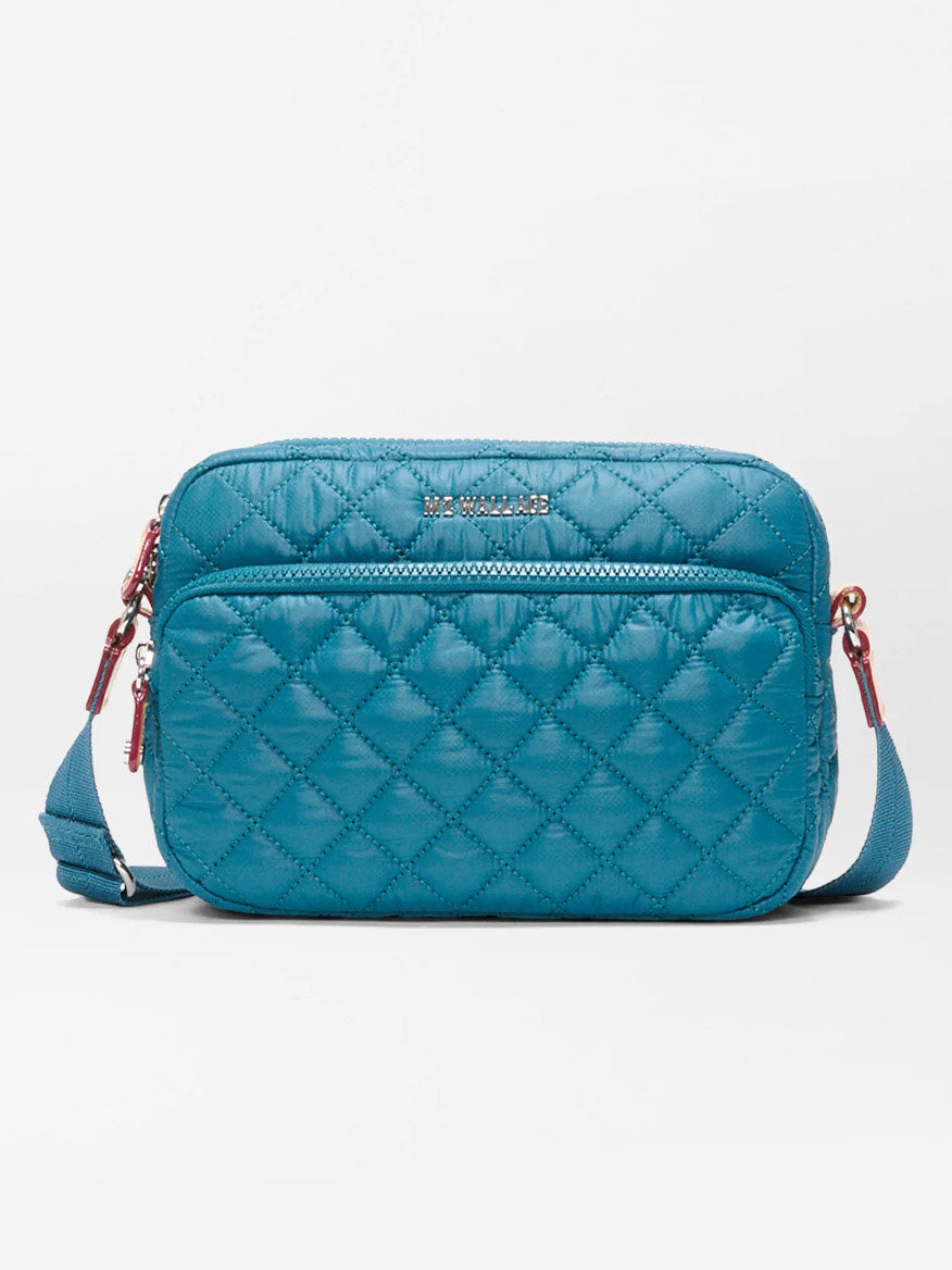 The MZ Wallace Small Metro Camera Bag in Pacific Oxford is a teal quilted nylon crossbody with zip closure, adjustable strap, and metal hardware, shown against a plain white background.