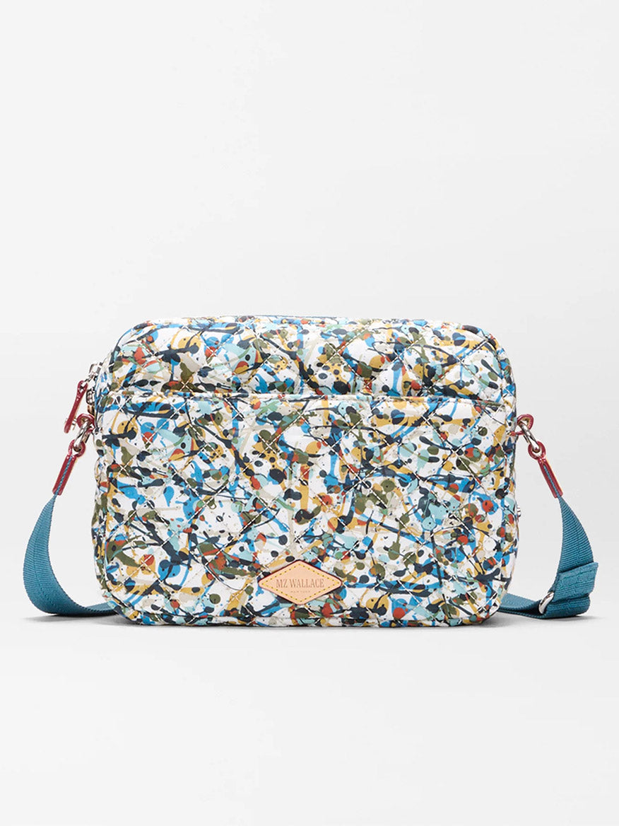 The MZ Wallace Small Metro Camera Bag in Club Paint Oxford features a rectangular nylon design with a blue strap and a multicolored abstract pattern, displayed against a white background.