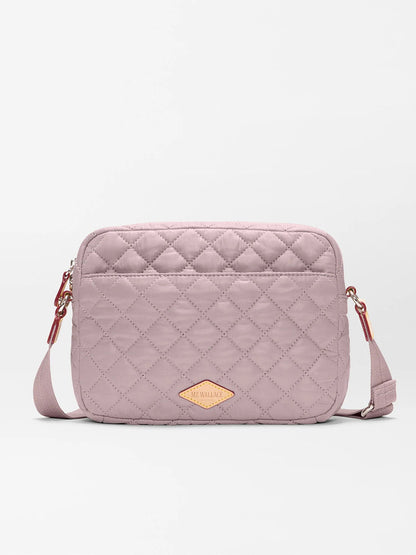 The MZ Wallace Small Metro Camera Bag in Quail Oxford is a rectangular, quilted light mauve crossbody bag with an adjustable strap and tan logo patch—ideal for hands-free style.