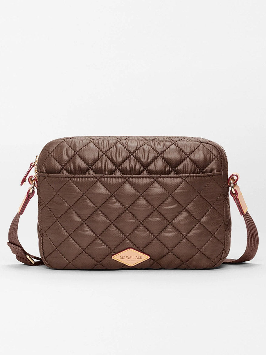 The MZ Wallace Small Metro Camera Bag in Walnut Oxford is a quilted brown crossbody with a rectangular shape, gold-tone hardware, and an adjustable strap for hands-free carry, crafted from recycled nylon and set against a plain white background.