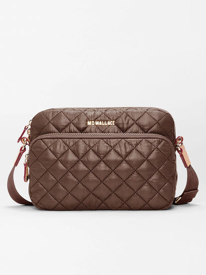 The MZ Wallace Small Metro Camera Bag in Walnut Oxford is crafted from recycled nylon in a brown quilted design, featuring a front zipper pocket, gold hardware, an adjustable strap for hands-free carry, and the “MZ WALLACE” logo on the front.