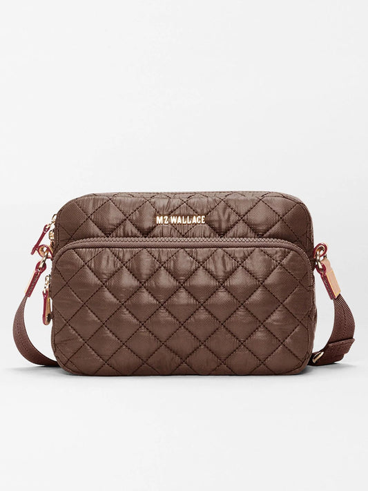 The MZ Wallace Small Metro Camera Bag in Walnut Oxford is crafted from recycled nylon in a brown quilted design, featuring a front zipper pocket, gold hardware, an adjustable strap for hands-free carry, and the “MZ WALLACE” logo on the front.
