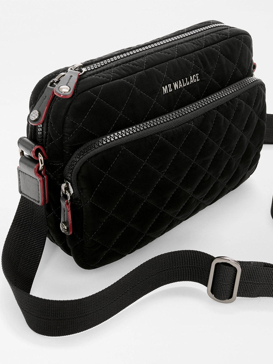 Small black quilted MZ Wallace Small Metro Camera Bag in Black Velvet Finish with a front zipper pocket, an adjustable strap, and red trim accents.