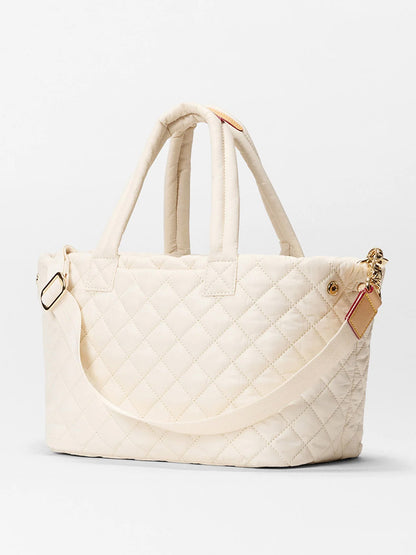 The MZ Wallace Small Metro City Tote in Sandshell Oxford features a cream quilted design, Italian leather trim, two short handles, and an adjustable crossbody strap, shown against a plain light background.