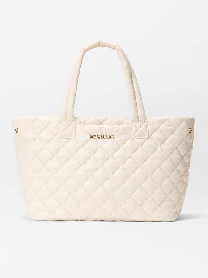 The MZ Wallace Small Metro City Tote in Sandshell Oxford features a quilted cream design, two handles, "MZ WALLACE" gold lettering on the front, and elegant Italian leather trim.