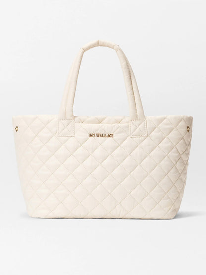 The MZ Wallace Small Metro City Tote in Sandshell Oxford features a quilted cream design, two handles, "MZ WALLACE" gold lettering on the front, and elegant Italian leather trim.