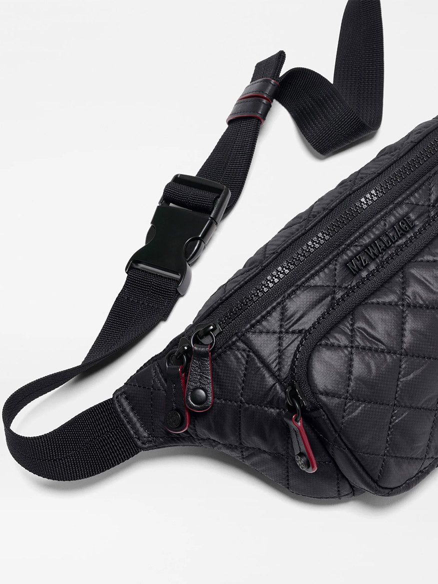 Close-up of the MZ Wallace Small Metro Sling in Black Oxford, featuring a quilted design, two zippered compartments, a black crossbody strap, Italian leather trim, and plastic buckle on a white background.