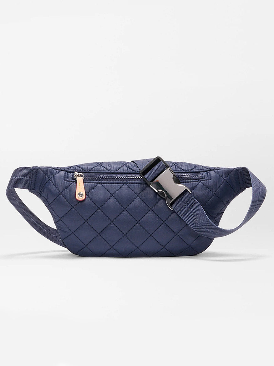 The MZ Wallace Small Metro Sling in Dawn Oxford is a navy blue quilted fanny pack with a front zipper pocket, adjustable crossbody strap, and plastic buckle, made from bluesign approved materials, shown on a plain white background.