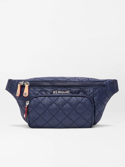 The MZ Wallace Small Metro Sling in Dawn Oxford is a navy quilted belt bag with front zip pockets, Italian leather trim, an adjustable crossbody strap, and "MZ WALLACE" branding on the main pocket.