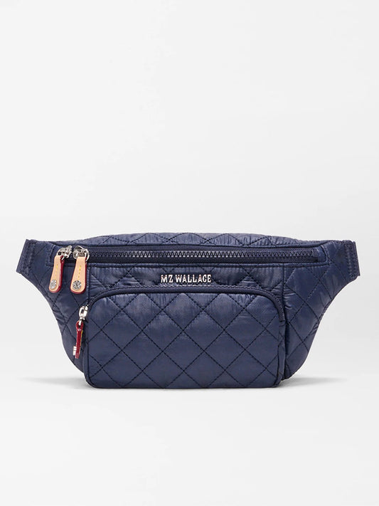The MZ Wallace Small Metro Sling in Dawn Oxford is a navy quilted belt bag with front zip pockets, Italian leather trim, an adjustable crossbody strap, and "MZ WALLACE" branding on the main pocket.