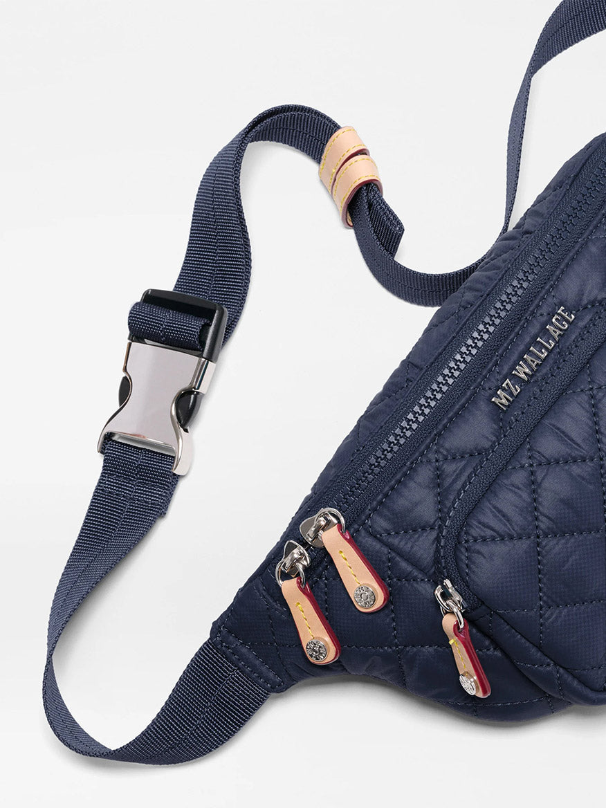 Close-up of the MZ Wallace Small Metro Sling in Dawn Oxford, a navy quilted crossbody bag with a silver buckle, three zippered pockets, "MZ WALLACE" branding, and a comfortable adjustable strap.