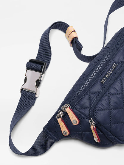 Close-up of the MZ Wallace Small Metro Sling in Dawn Oxford, a navy quilted crossbody bag with a silver buckle, three zippered pockets, "MZ WALLACE" branding, and a comfortable adjustable strap.