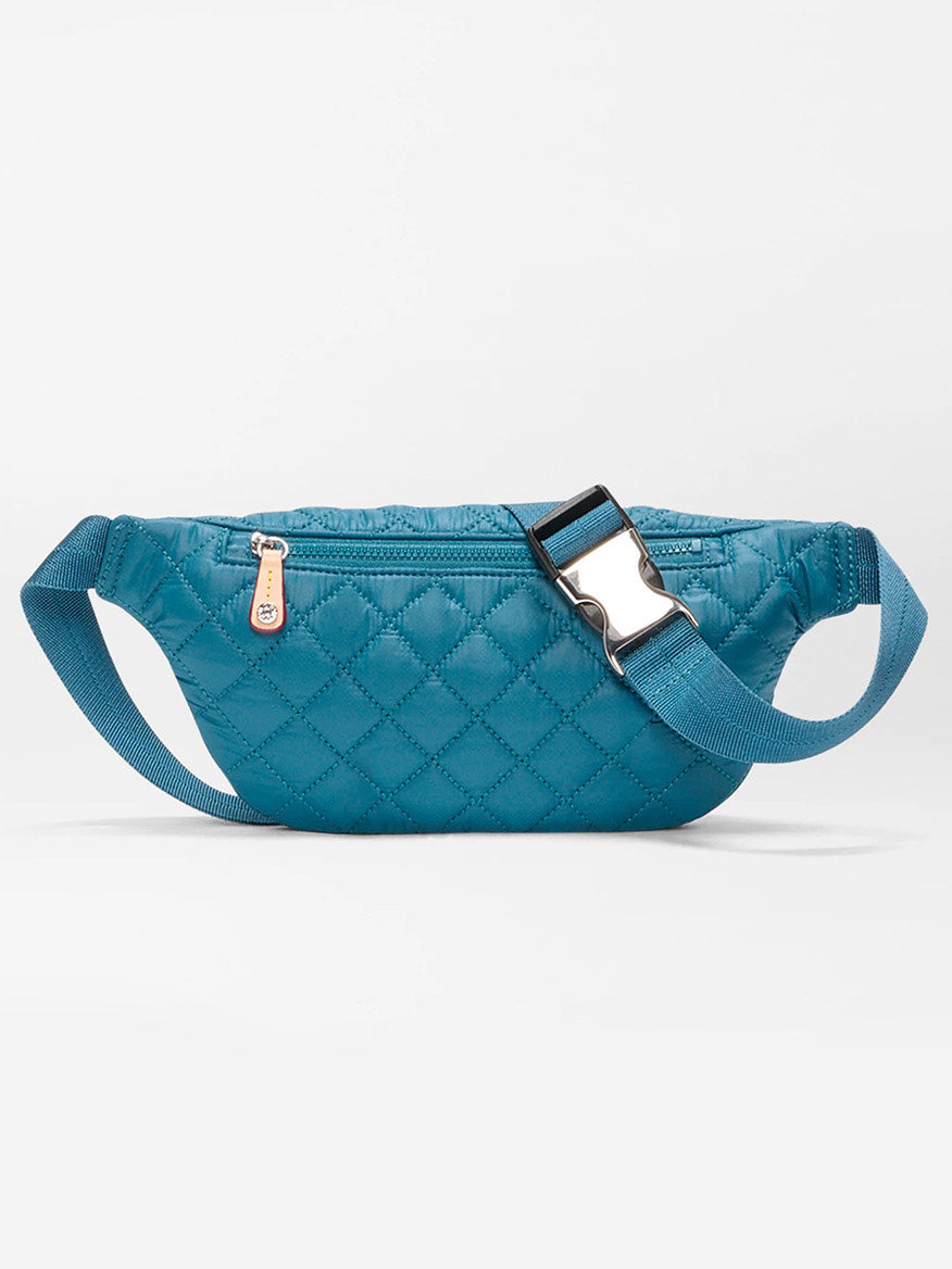 The MZ Wallace Small Metro Sling in Pacific Oxford is a blue quilted belt bag with an adjustable crossbody strap, side zipper, silver buckle, and Italian leather trim, shown against a plain white background.