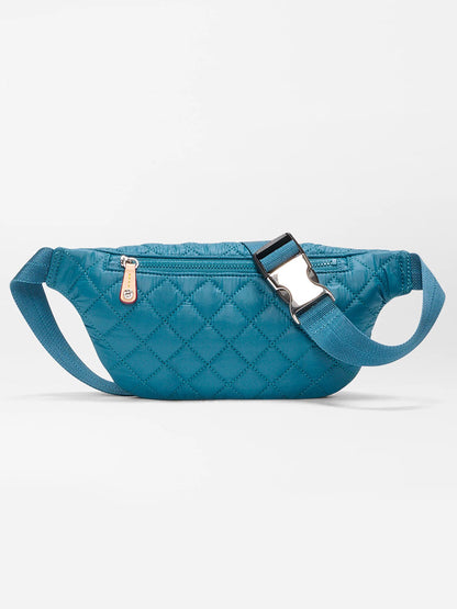 The MZ Wallace Small Metro Sling in Pacific Oxford is a blue quilted belt bag with an adjustable crossbody strap, side zipper, silver buckle, and Italian leather trim, shown against a plain white background.