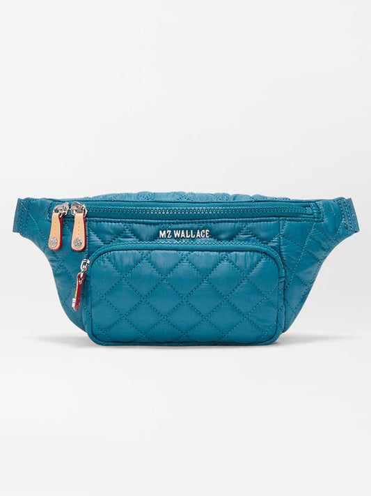The MZ Wallace Small Metro Sling in Pacific Oxford is a blue quilted belt bag featuring a front zip pocket, Italian leather trim, leather zipper pulls, and "MZ WALLACE" branding on the front.