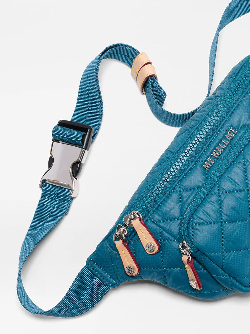 Close-up of the MZ Wallace Small Metro Sling in Pacific Oxford, featuring blue quilted nylon, three zippered pockets, Italian leather trim and zipper pulls, plus an adjustable crossbody strap with a silver buckle.