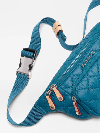 Close-up of the MZ Wallace Small Metro Sling in Pacific Oxford, featuring blue quilted nylon, three zippered pockets, Italian leather trim and zipper pulls, plus an adjustable crossbody strap with a silver buckle.