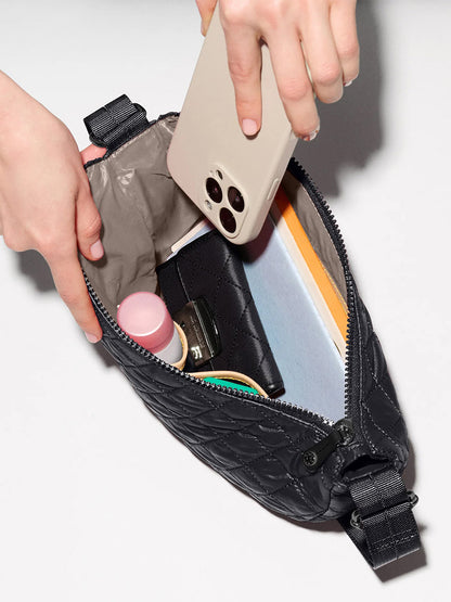 Someone slips a smartphone into an open MZ Wallace Small Metro Smile Bag in Black Oxford, which holds a notebook, cosmetics, and small personal items.
