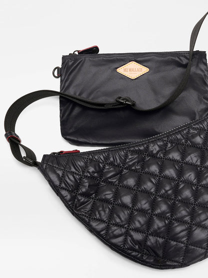 Shown are two black MZ Wallace bags: the Small Metro Smile Bag in Black Oxford with a quilted, curved design, and another flat, rectangular bag featuring a small logo patch.