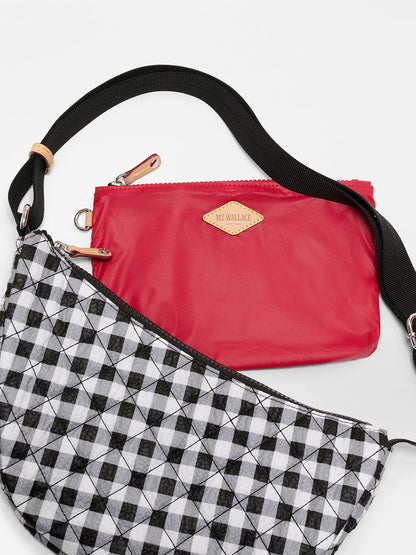 Two bags are shown: one is red with a gold MZ Wallace label and Italian leather trim, the other is the MZ Wallace Small Metro Smile Bag in Black/White Gingham Oxford with a geometric pattern and adjustable nylon strap.