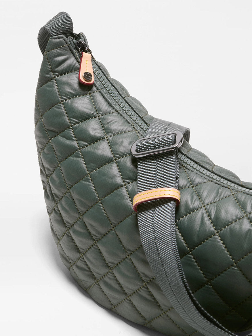 Close-up of the MZ Wallace Small Metro Smile Bag in Juniper Oxford—a quilted dark green crossbody crafted from recycled nylon, featuring a zippered top closure, black strap, and a tan leather accent on the buckle.