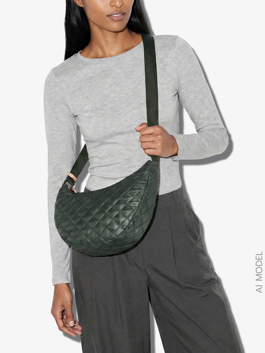 A person wearing a light grey long-sleeve shirt and dark grey pants carries the MZ Wallace Small Metro Smile Bag in Juniper Oxford, crafted from recycled nylon.