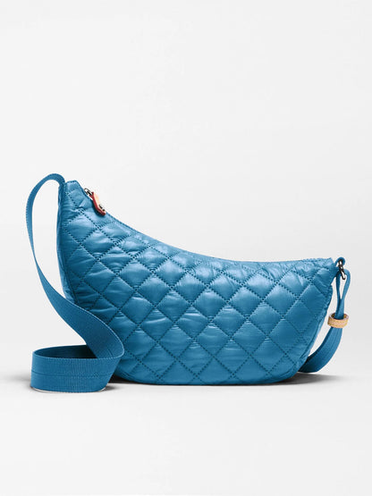 MZ Wallace Small Metro Smile Bag in Atlantic Blue Oxford, featuring a quilted design, adjustable strap, rounded crescent shape, and zipper closure, displayed against a plain white background.