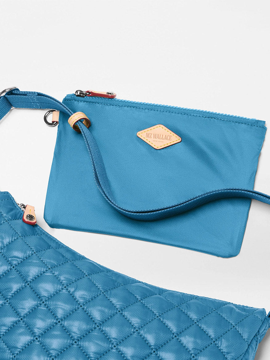 Two blue MZ Wallace bags are shown: the Small Metro Smile Bag in Atlantic Blue Oxford, crafted from recycled oxford nylon with a tan logo patch, and a larger quilted bag with a crossbody strap—perfect for everyday carry.