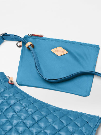 Two blue MZ Wallace bags are shown: the Small Metro Smile Bag in Atlantic Blue Oxford, crafted from recycled oxford nylon with a tan logo patch, and a larger quilted bag with a crossbody strap—perfect for everyday carry.