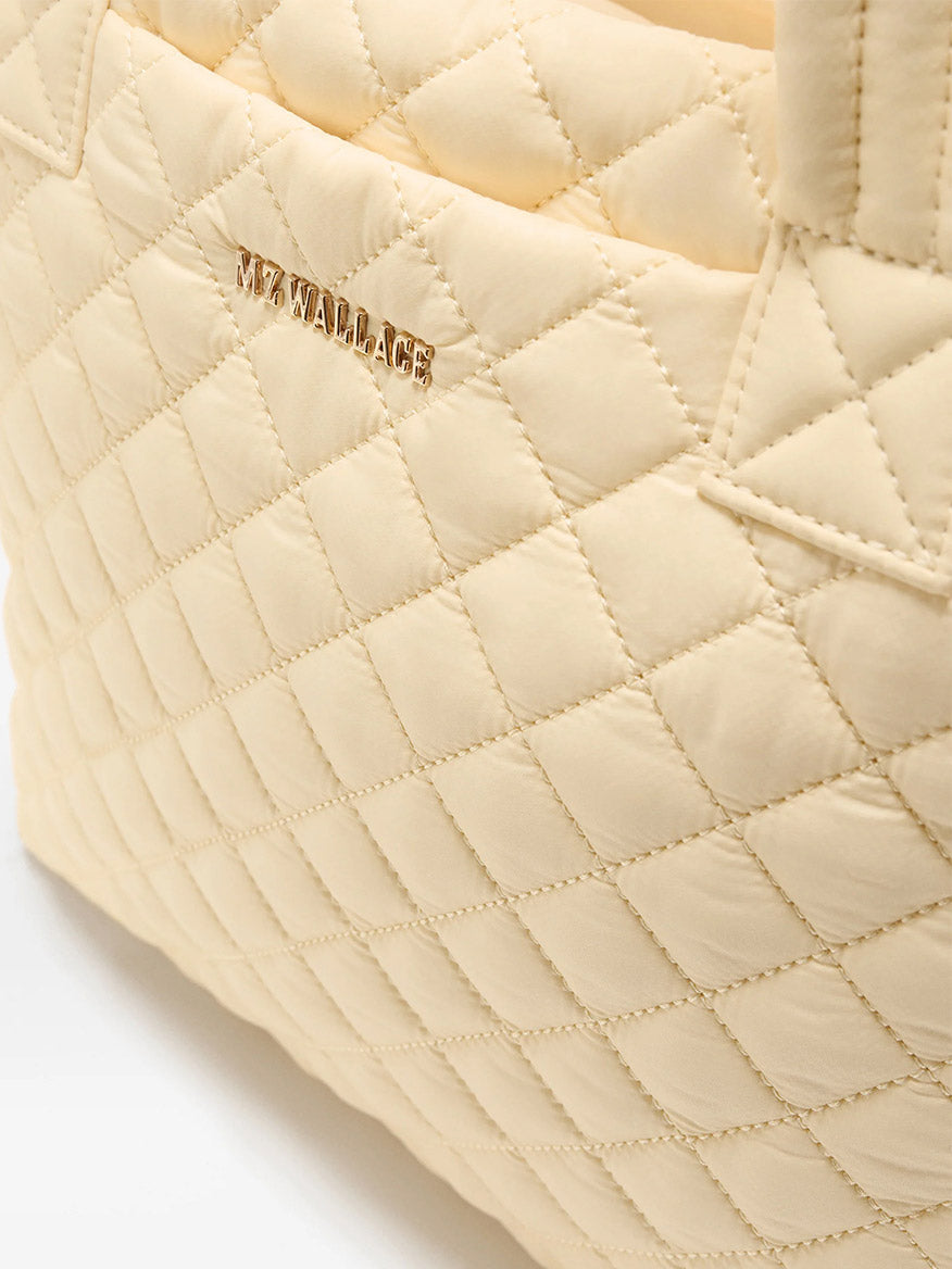 Close-up of the MZ Wallace Small Metro Tote Deluxe in Chamomile Oxford, featuring a quilted finish, gold "MZ WALLACE" logo, and elegant Italian leather trim.