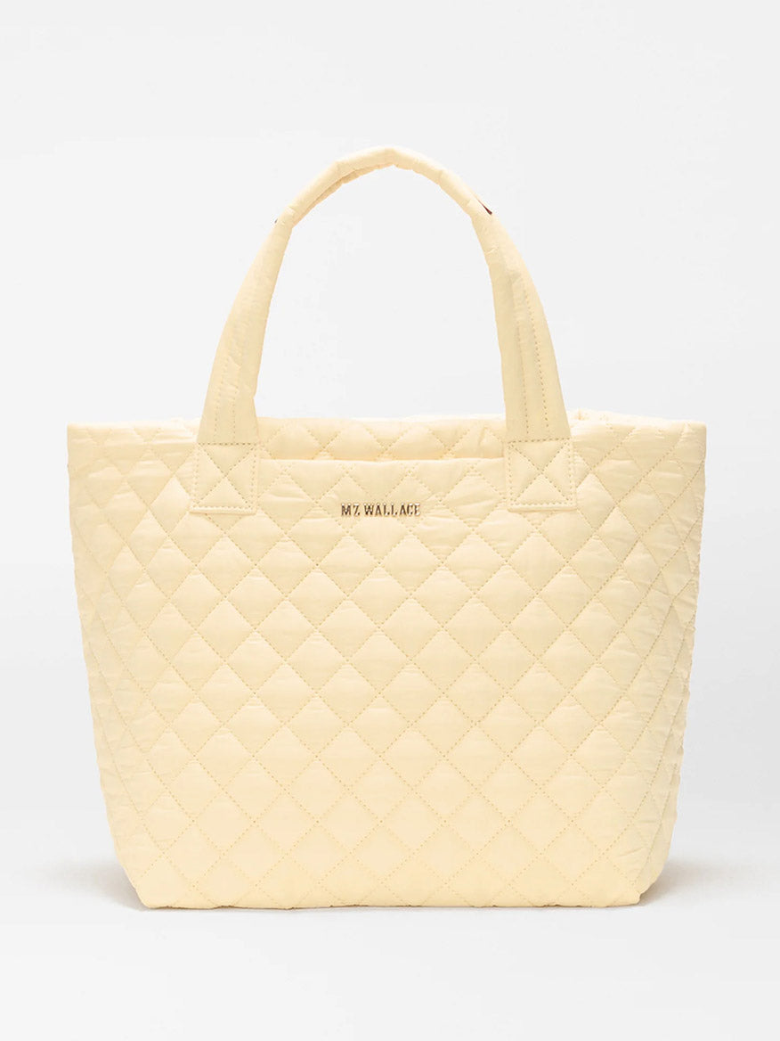 The MZ Wallace Small Metro Tote Deluxe in Chamomile Oxford is a light yellow quilted tote with Italian leather trim, two handles, and "MZ WALLACE" in gold on the front, shown against a plain white background.