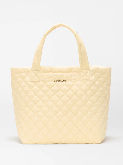 The MZ Wallace Small Metro Tote Deluxe in Chamomile Oxford is a light yellow quilted tote with Italian leather trim, two handles, and "MZ WALLACE" in gold on the front, shown against a plain white background.
