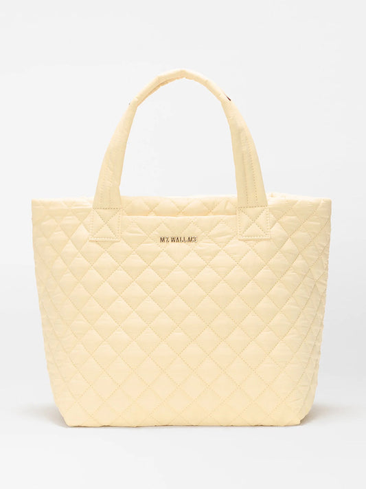 The MZ Wallace Small Metro Tote Deluxe in Chamomile Oxford is a light yellow quilted tote with Italian leather trim, two handles, and "MZ WALLACE" in gold on the front, shown against a plain white background.