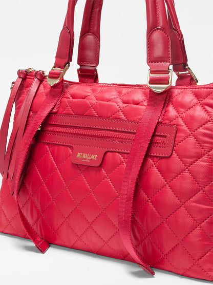 The MZ Wallace Small Park Satchel in Apple Oxford features a quilted red design, double handles, front zipper pocket, and gold-tone hardware—a stylish and practical choice for everyday use.