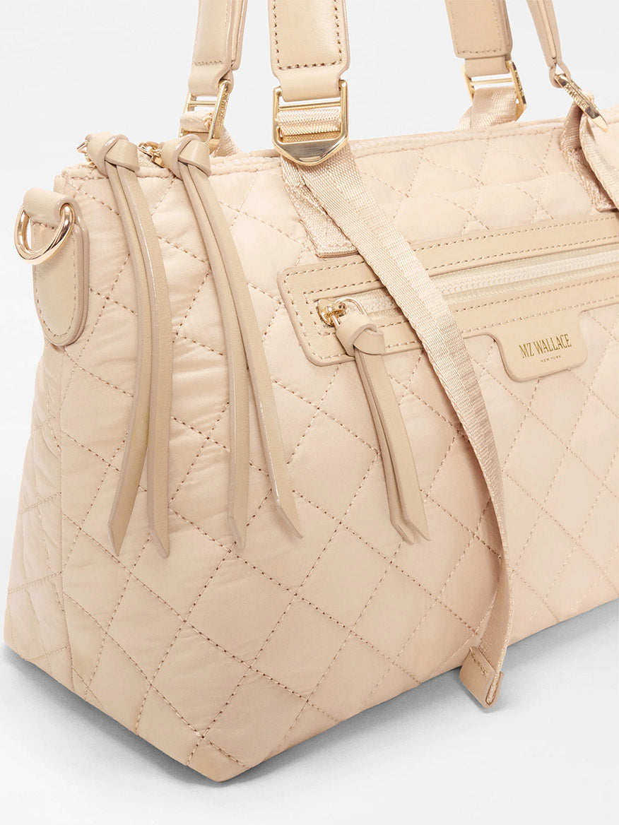 The MZ Wallace Small Park Satchel in Buff Oxford features beige quilted fabric, gold hardware, two zip pockets, shoulder straps, stitched diamond pattern, and a logo plaque—ideal for everyday use.