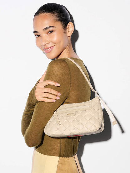 A woman in a light brown top smiles while posing against a white background, holding the MZ Wallace Small Park Shoulder Bag in Buff Oxford under her arm.