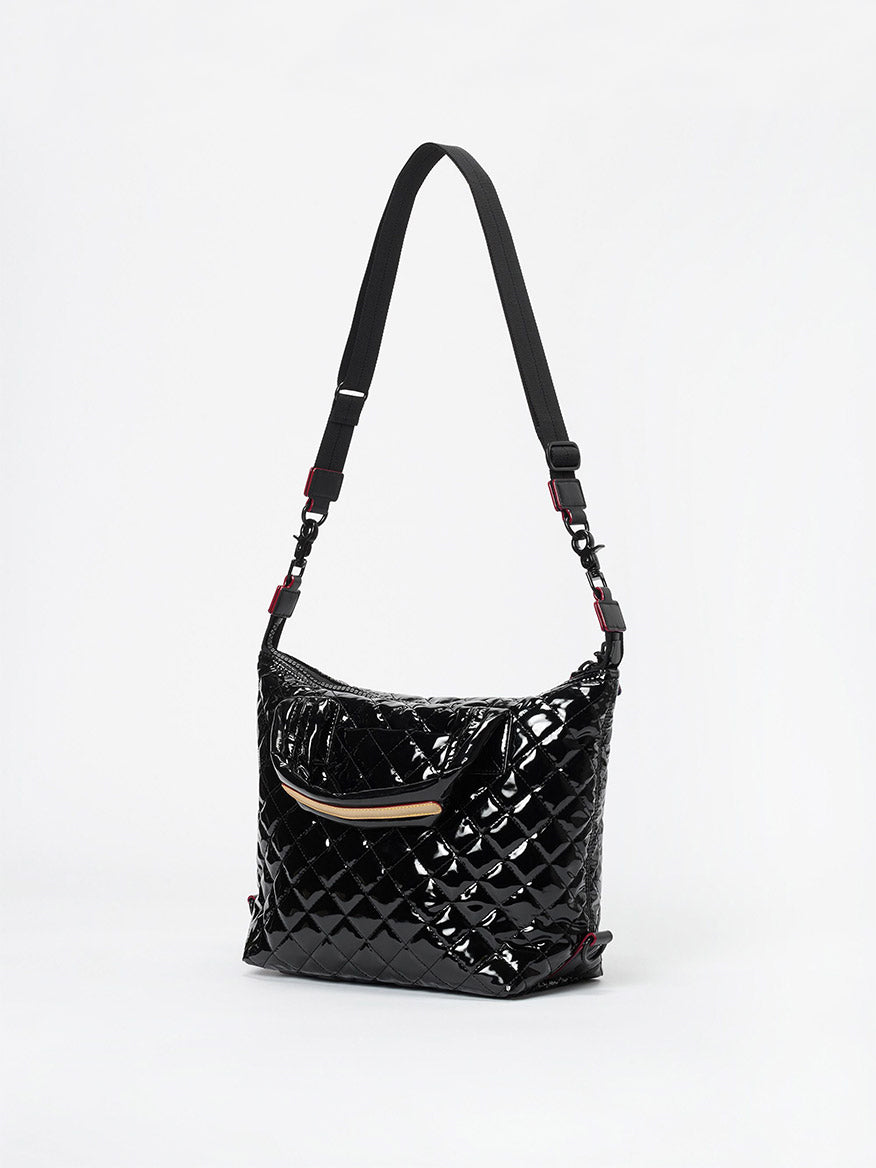 The MZ Wallace Small Sutton Deluxe in Black Lacquer Oxford, featuring a quilted design, front zip pocket, adjustable crossbody strap, shiny patent finish, and Italian leather trim, is displayed against a plain white background.