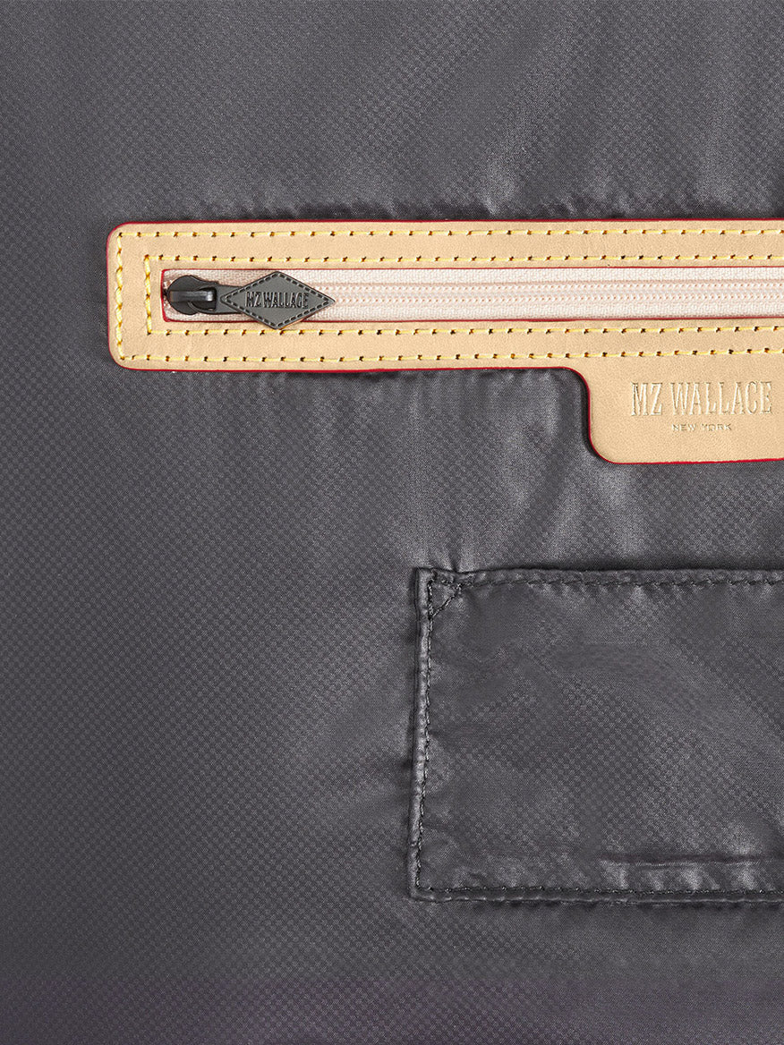 Close-up of the MZ Wallace Small Sutton Deluxe in Black Lacquer Oxford, showing its tan Italian leather-trimmed zippered pocket with metal pull and "MZ WALLACE" branding inside.