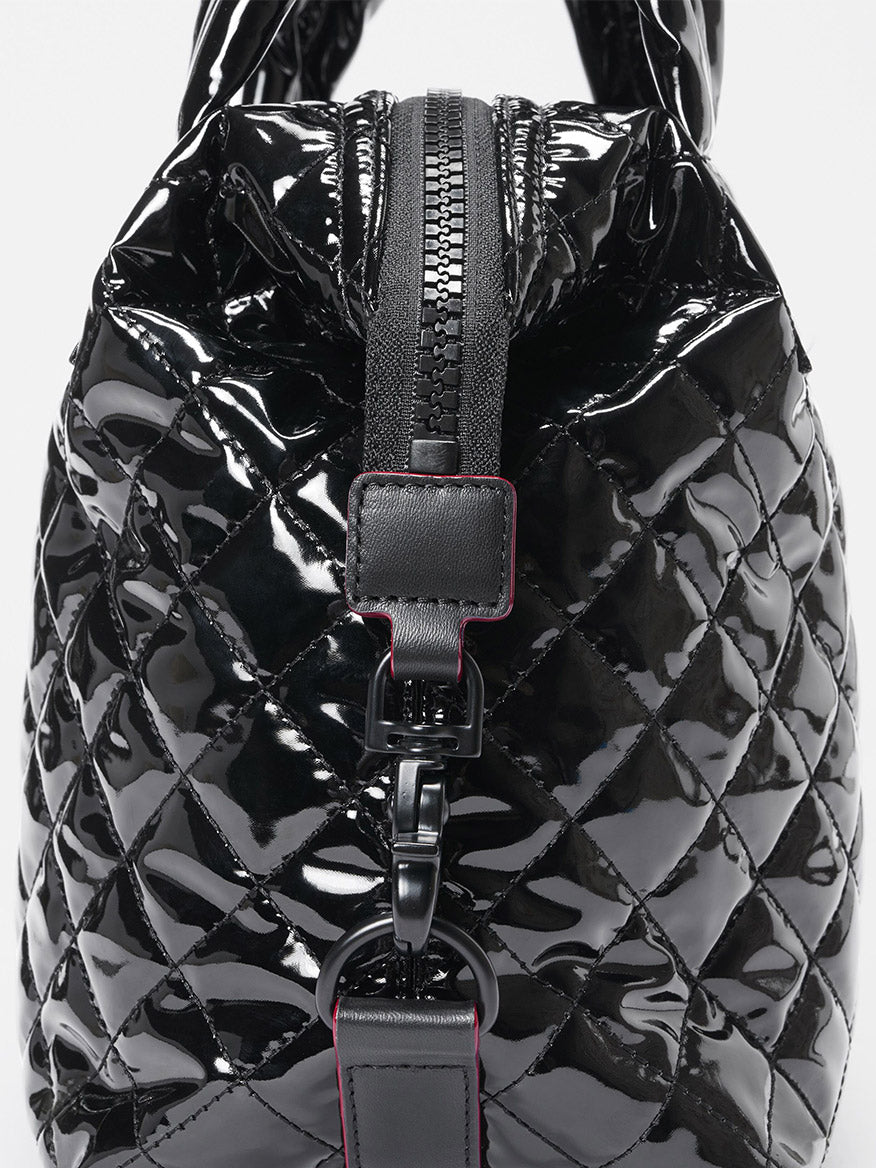 Close-up of the MZ Wallace Small Sutton Deluxe in Black Lacquer Oxford, featuring a glossy quilted finish, Italian leather trim, front zipper, and metal clasp.