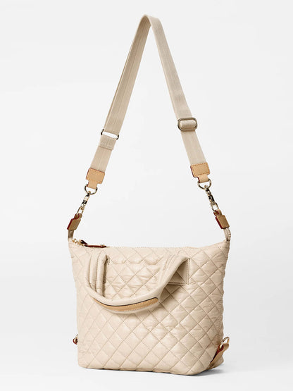 The MZ Wallace Small Sutton Deluxe in Buff Oxford features a chic quilted design with a stylish crossbody strap and adjustable top handles. Enhanced by elegant Italian leather trim, it maintains its luxury appeal even against a white background.