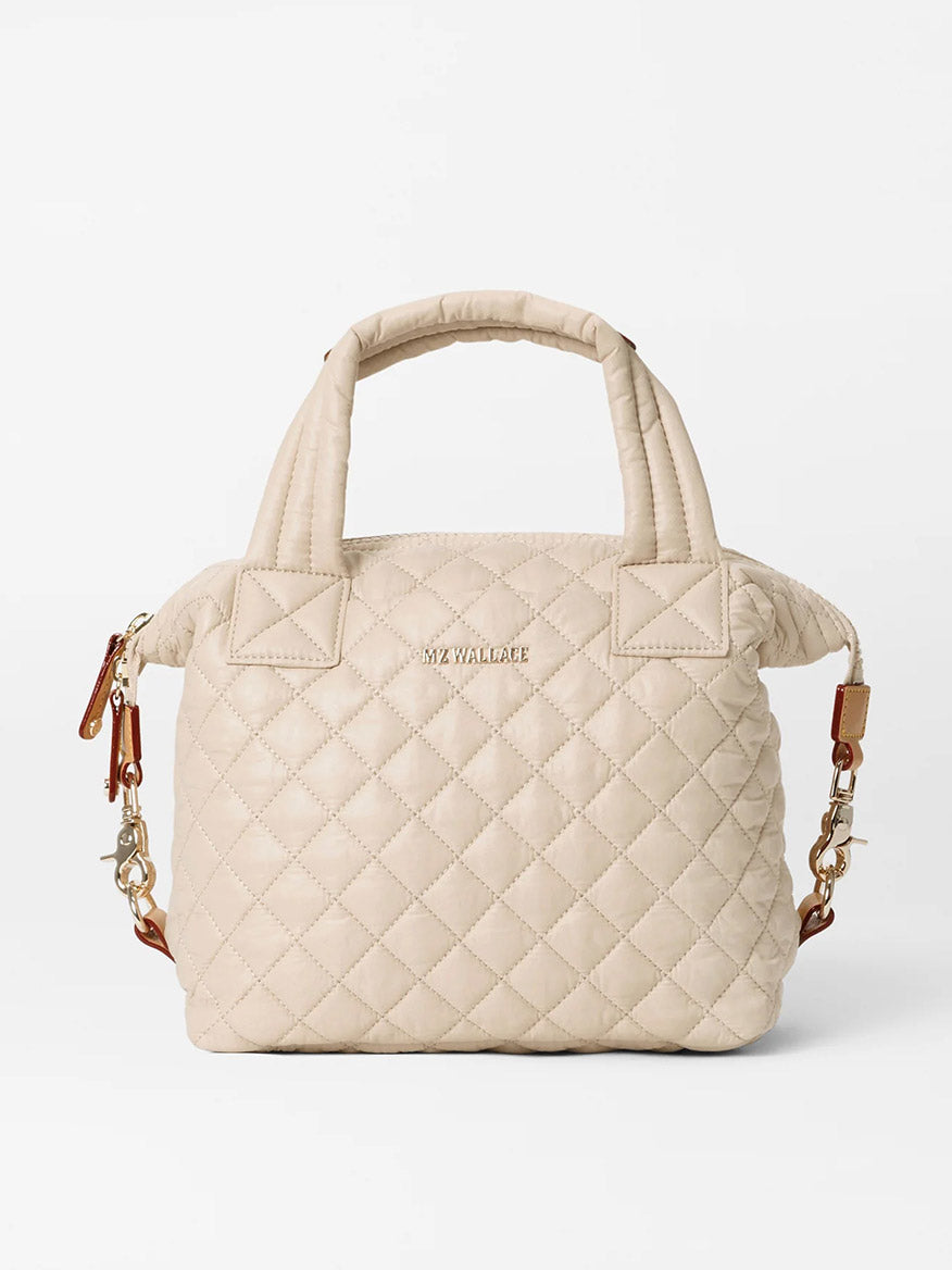 The MZ Wallace Small Sutton Deluxe in Buff Oxford is a beige quilted handbag with short handles and gold hardware, featuring a detachable brown crossbody strap, zipper closure, and elegant Italian leather trim for added luxury.